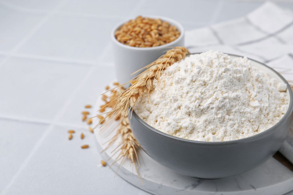 wheat flour grain and spikes on white tiled table